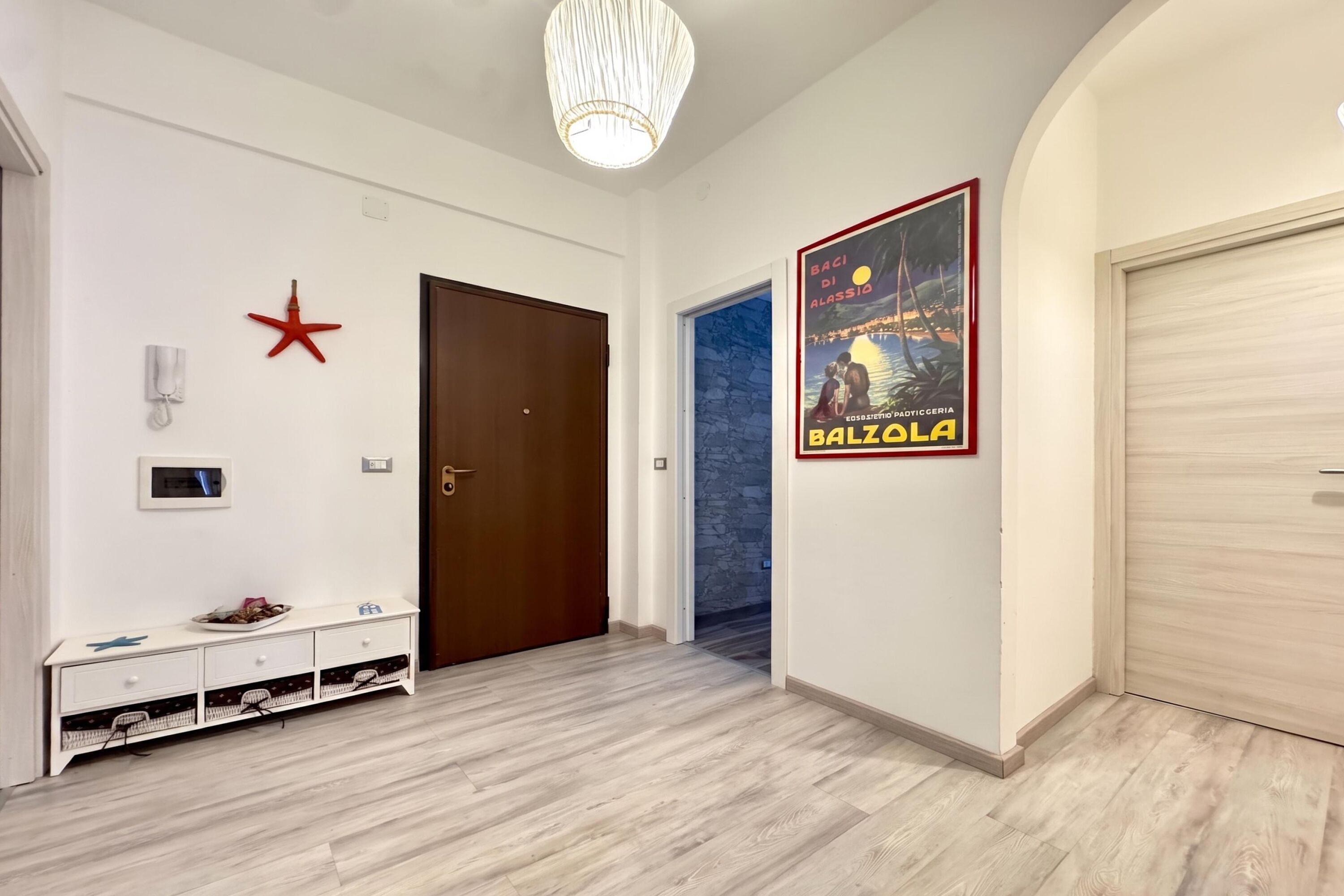 Un couloir avec un plancher en bois, une porte, une étoile rouge décorative fixée au mur, une console blanche avec un plateau, et une affiche accrochée au mur.
