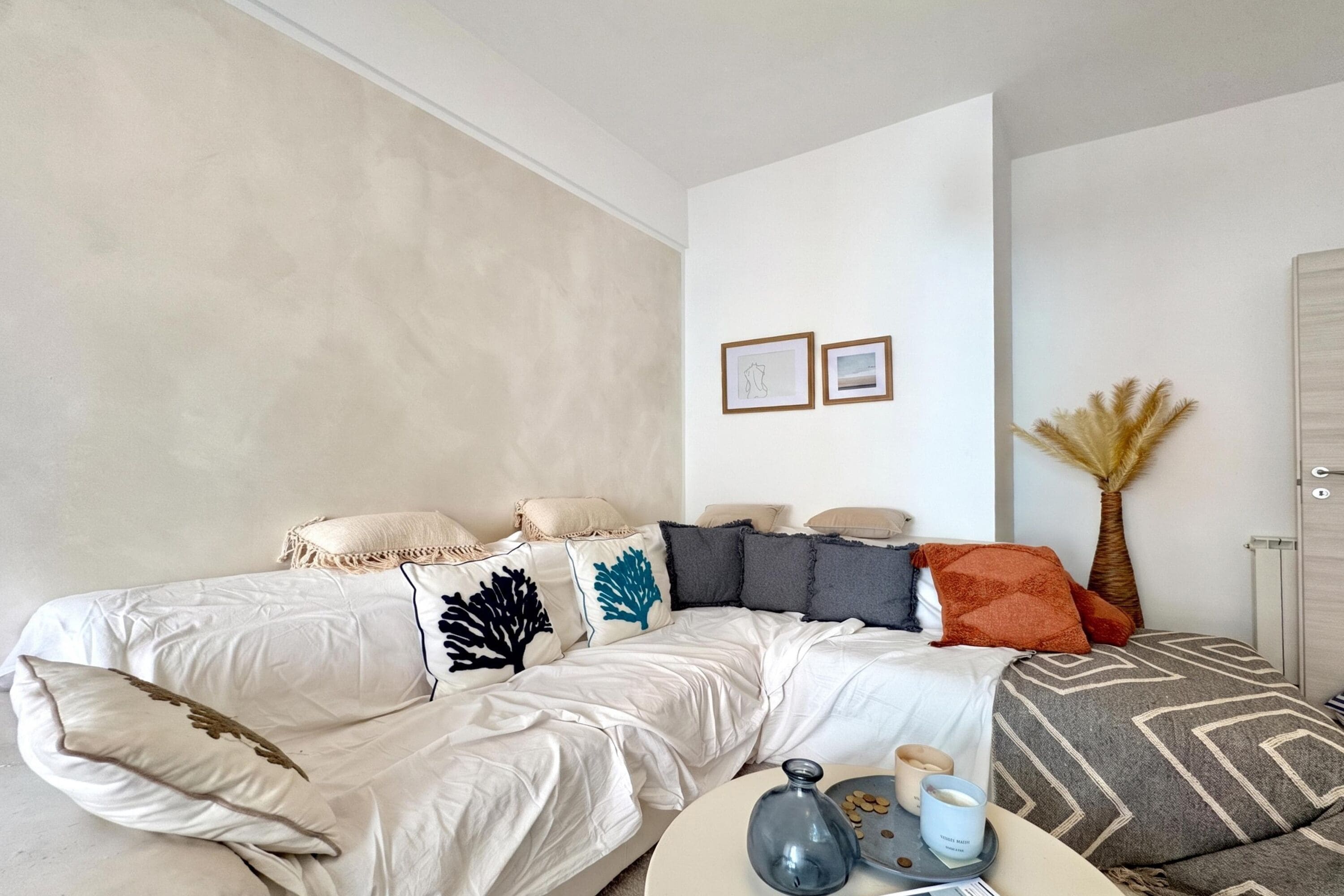 Un salon moderne avec un grand lit, une table basse ornée de bougies et un mur sur lequel sont accrochées deux images encadrées.