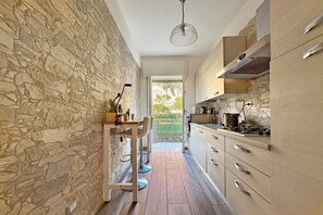 Une cuisine étroite aux murs en pierre, une table à manger en bois et une vue sur l’extérieur.