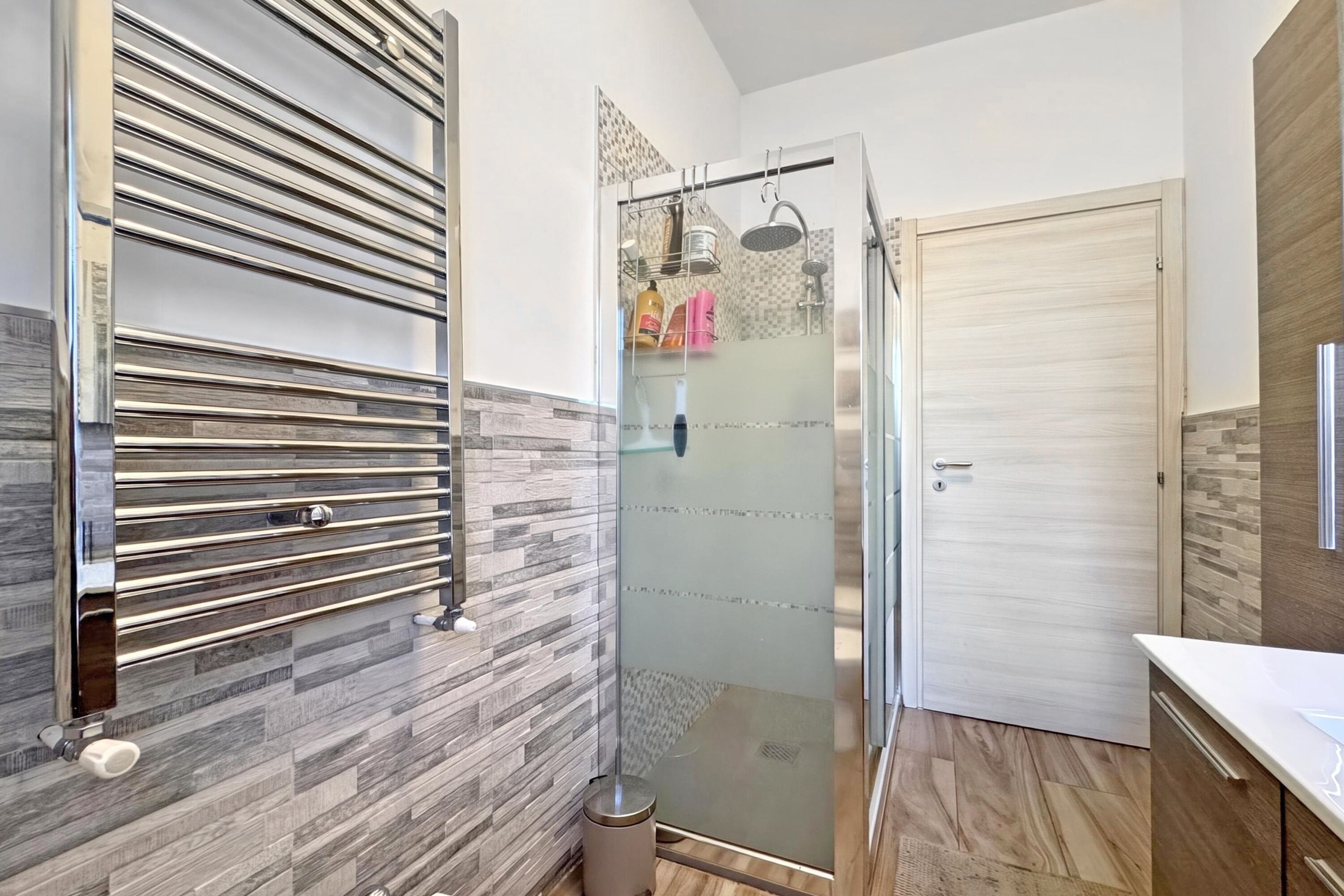 Un baño moderno con cabina de ducha de vidrio, tocador de madera y perchero.