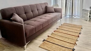 A brown sofa with a cushion, a woven rug, a chair, and a small table with a plant. - Le Conchiglie Di Grace - Apartment With Balcony (Alassio)