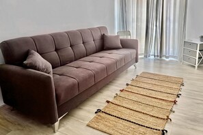 A brown sofa with a cushion, a woven rug, a chair, and a small table with a plant. - Le Conchiglie Di Grace - Apartment With Balcony (Alassio)