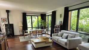 Un salon moderne doté d’une cheminée, d’une table à manger et de grandes fenêtres offrant une vue sur la verdure.