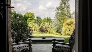 Patio aperto con due poltrone decorate, un tavolo e vista su un giardino curato, ricco di piante e prato.