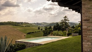 Una piscina con bordo in pietra, circondata da un prato e un muro in mattoni.