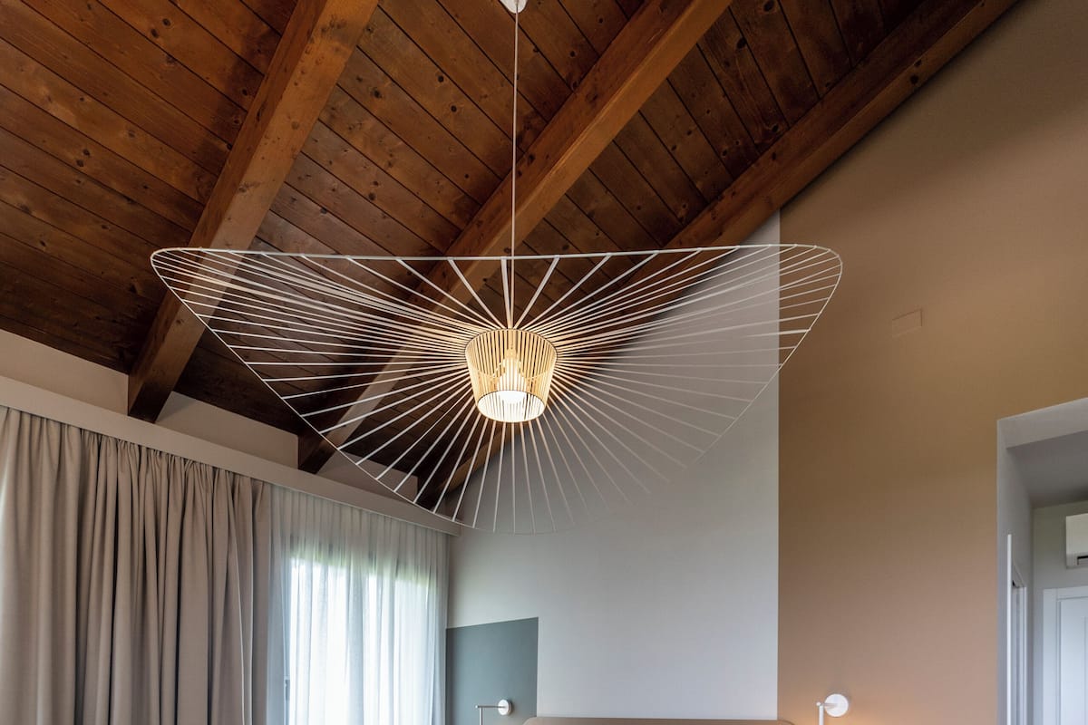 Ett sovrum med ett träpanelat tak, en säng med ett grönt överkast, ett sängbord och en väggmonterad lampa.