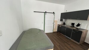 Quarto compacto com cama, cozinha compacta e porta com toalha pendurada.