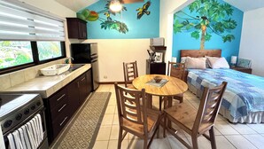 Una cocina compacta con comedor, ventilador de techo y un mural de un árbol con frutos.