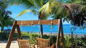 Un columpio de madera con dos columpios, una palmera y vista al mar con barcos.