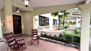 Un patio techado con una hamaca, mecedoras y un ventilador de techo.
