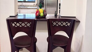 Una cocina con dos sillas de madera oscura, un refrigerador de acero inoxidable y un frutero sobre la encimera.
