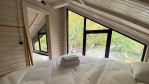 Ein Schlafzimmer mit einem großen Bett, einem Fenster mit Blick auf Bäume und einer Holzzieldecke.