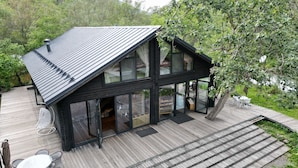 Ein modernes Haus mit großer Terrasse, Glasüren und Blick auf die umliegende Natur.