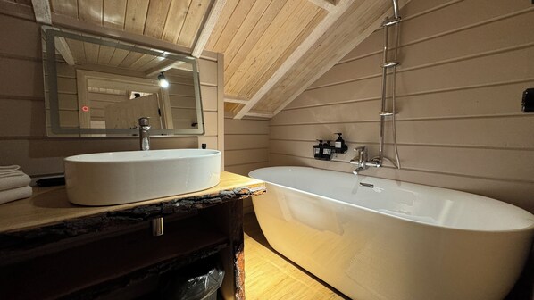 A modern bathroom with a freestanding bathtub, a large mirror, and wooden paneling on the walls. - Turgensai Hotel (Leskhoz)