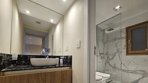 Un baño moderno con un espejo grande, un lavamanos sobre encimera, armarios de madera, una ducha con cerramiento de vidrio y suelo de mármol.