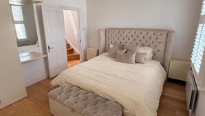 Ein Schlafzimmer mit einem großen Bett, einer Bank, einem Nachttisch und einer Tür, die zu einer Treppe führt.