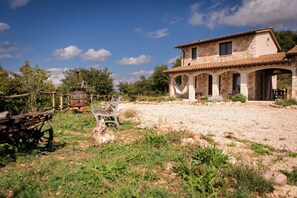 A rustic stone house with a tiled roof, a gravel driveway, and a bench.