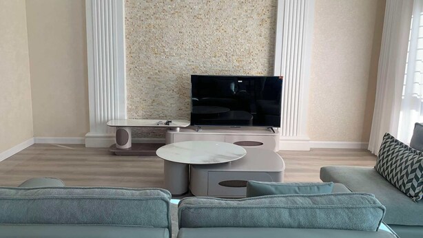 Ett modernt vardagsrum med en platt-TV, ett soffbord i marmor och en grå soffa.