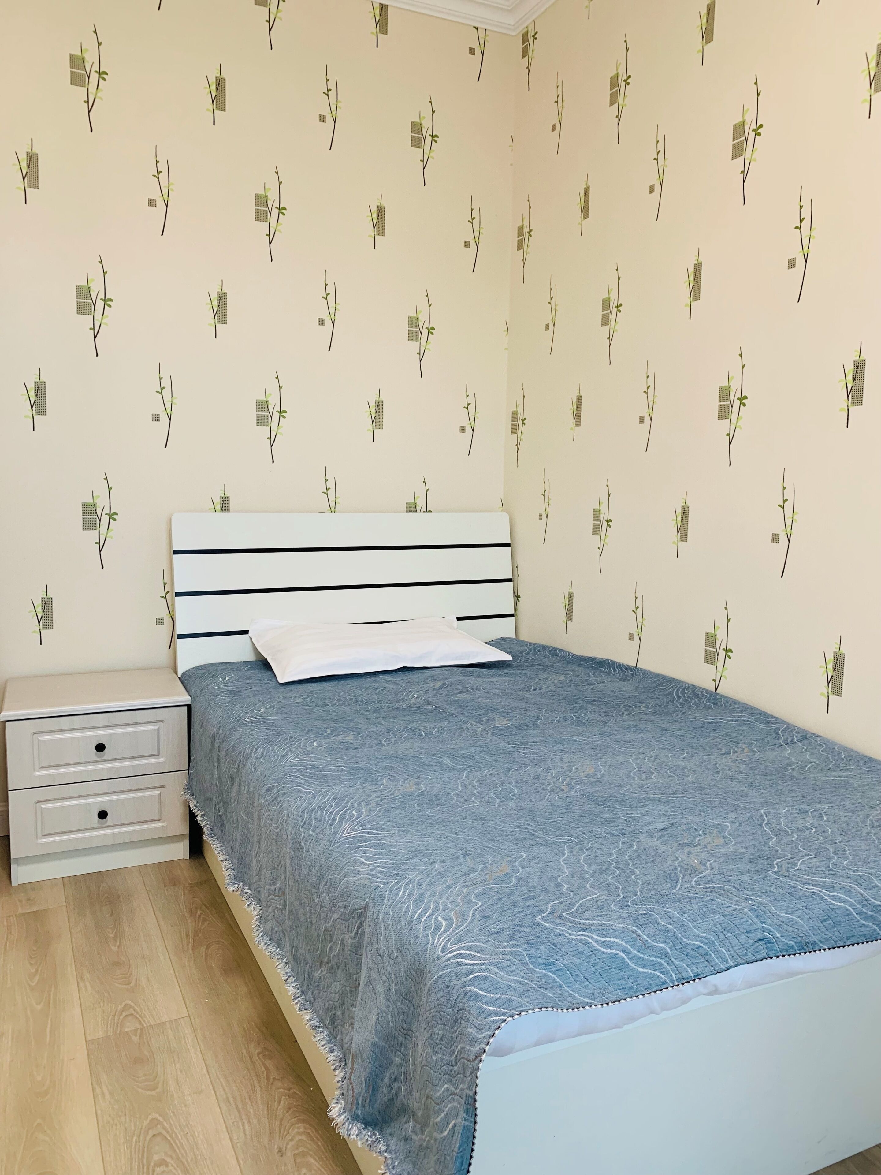 Makuuhuone, jossa on sänky, yöpöytä ja seinä, jonka kuvioinnissa on oksia ja lehtiä.