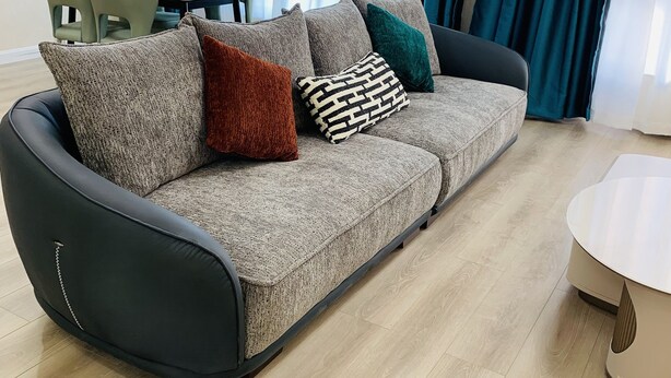 Un salon moderne avec un canapé gris, de nombreux coussins, une table basse ronde et un coin repas comprenant des chaises et une table.