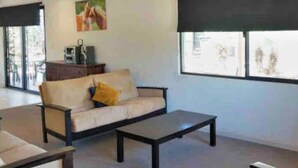 Un salon moderne avec un canapé, une table basse et une grande fenêtre équipée de stores.