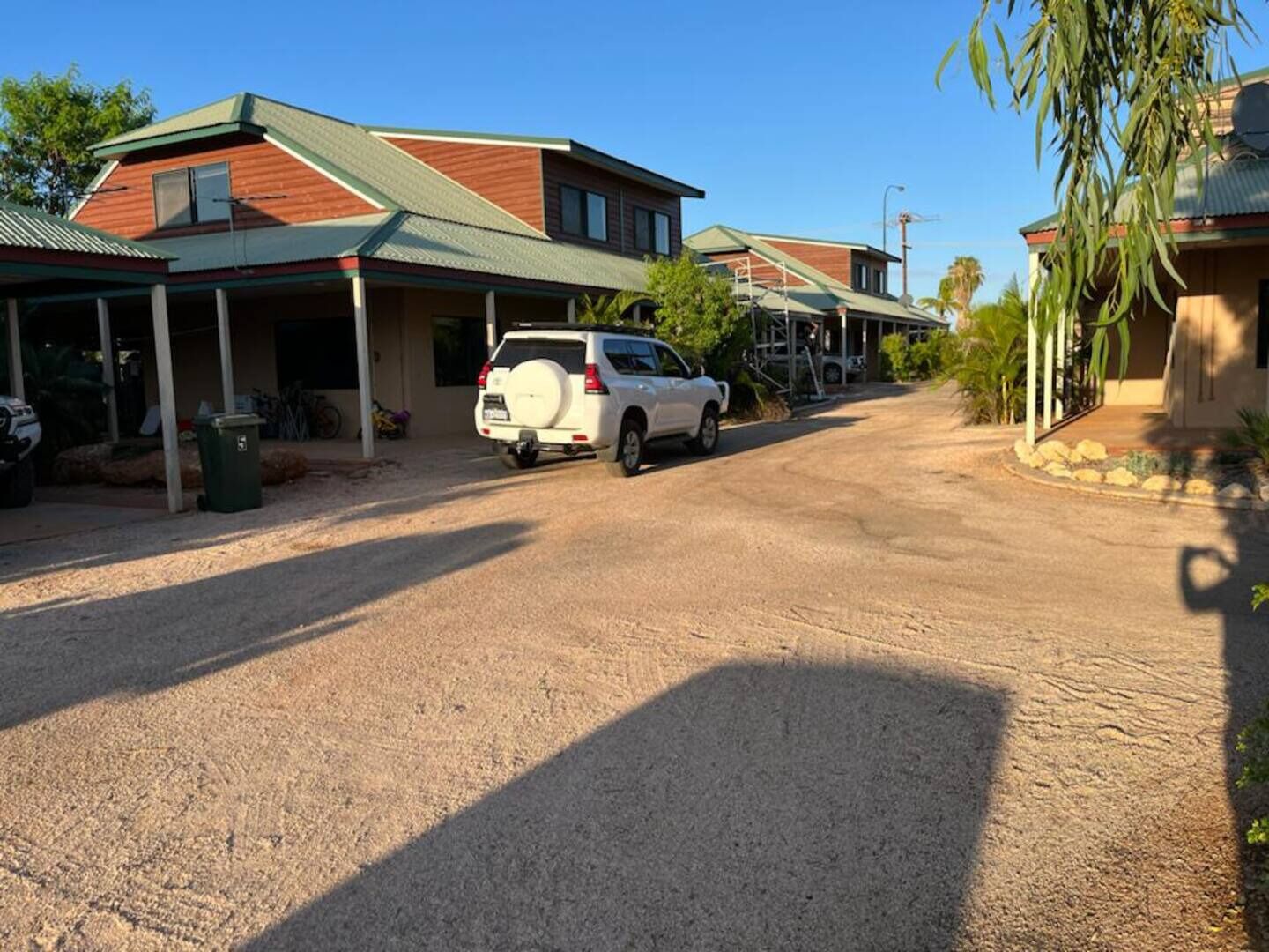 A residential street with houses, a white SUV parked on the side, and a clear blue sky.