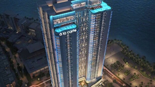 A high-rise hotel with a prominent 'la carte' sign, surrounded by water and greenery. - Alacarte Ha Long - Ha Apartment (Bai Chay)