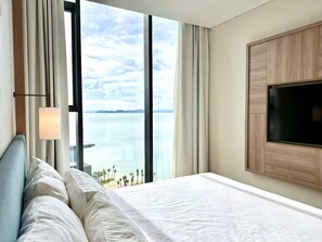 A hotel room with a large bed, a TV mounted on the wall, and a view of the sea through large windows. - Alacarte Ha Long - Ha Apartment (Bai Chay)