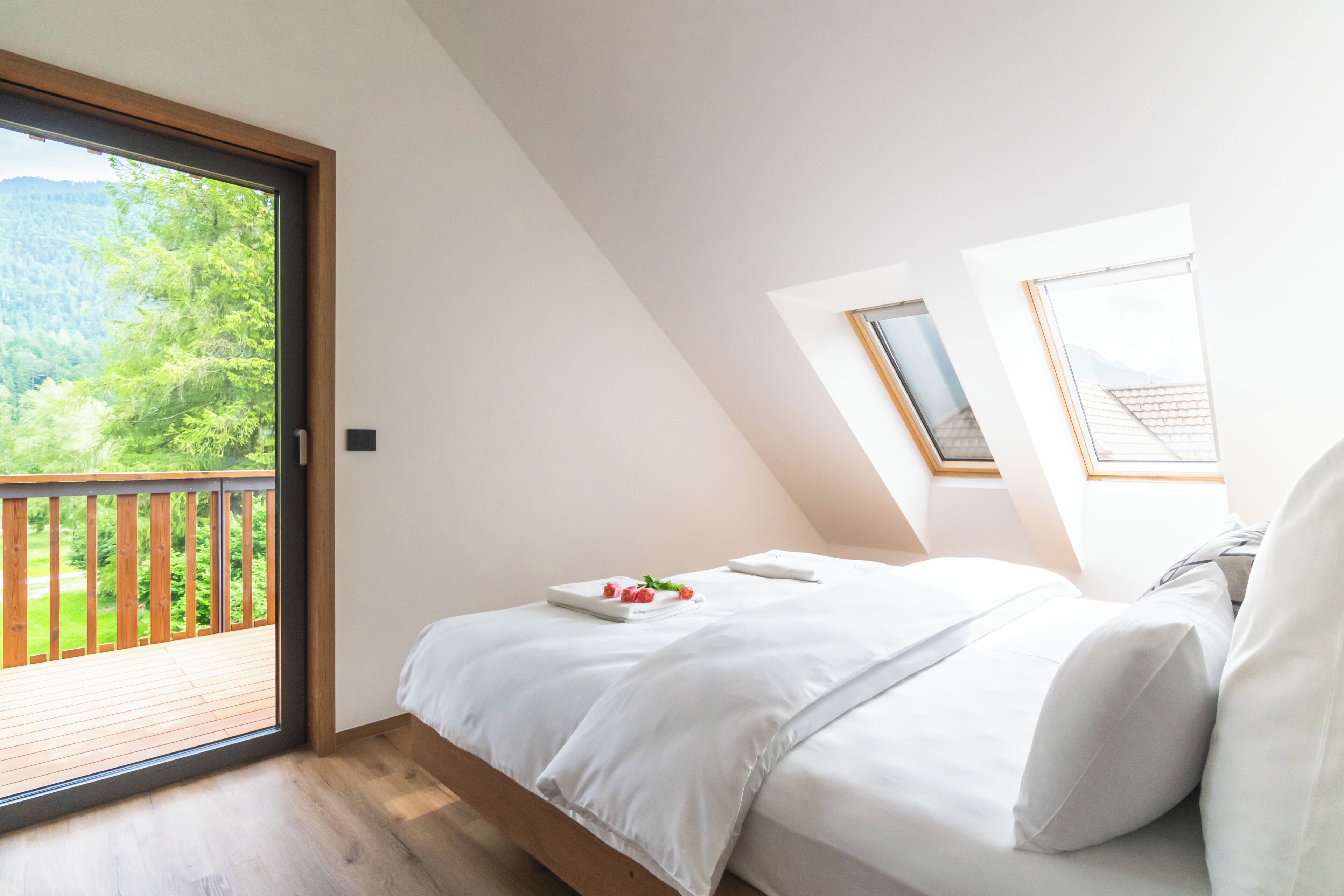 Een slaapkamer met een groot raam, een houten terras en een bed met witte lakens.