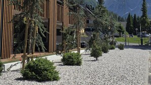 Ein modernes Gebäude mit Holzverkleidung und einem Kieshof, umgeben von Bäumen und Bergen im Hintergrund.