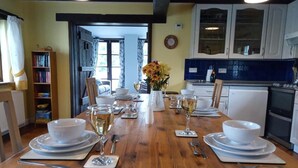 Une salle à manger avec une table en bois dressée pour quatre personnes, des assiettes blanches, des verres à vin et un vase rempli de fleurs.