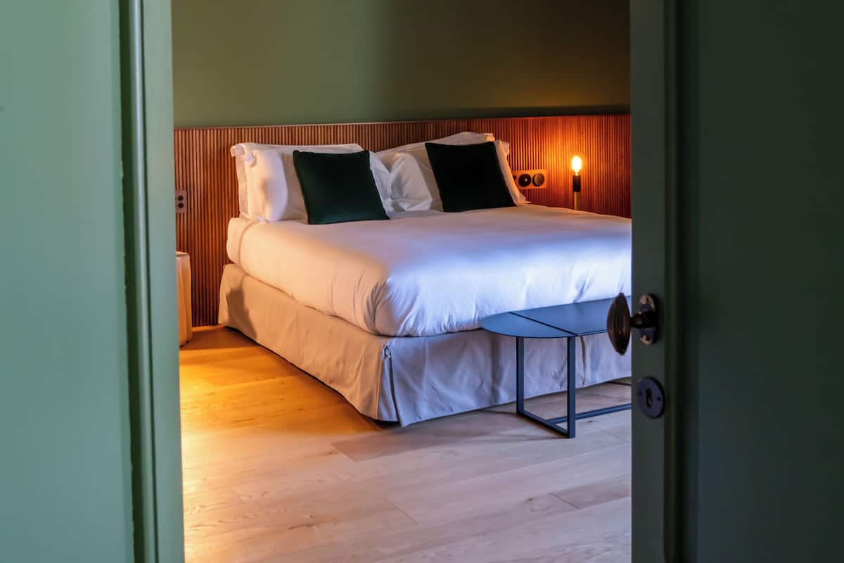 A hotel room with a bed, bedside table, and a wall-mounted lamp.