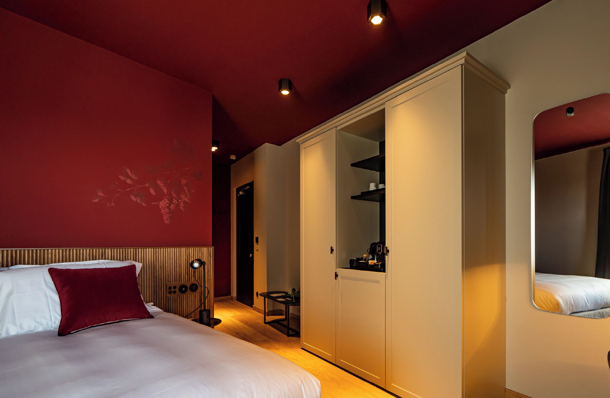 A hotel room with a bed, a wardrobe, a mirror, and a small table with a plant.