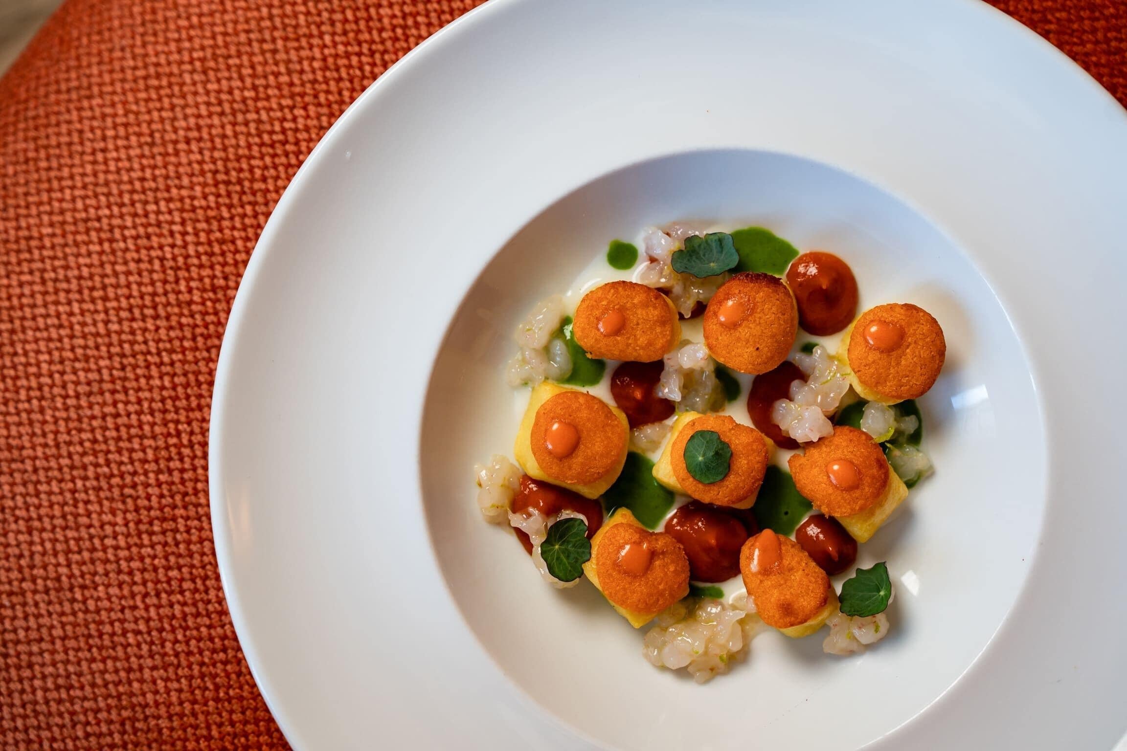 Een wit bord met een gerecht bestaande uit rijst, groene bladeren en ronde, bruin-gouden items.