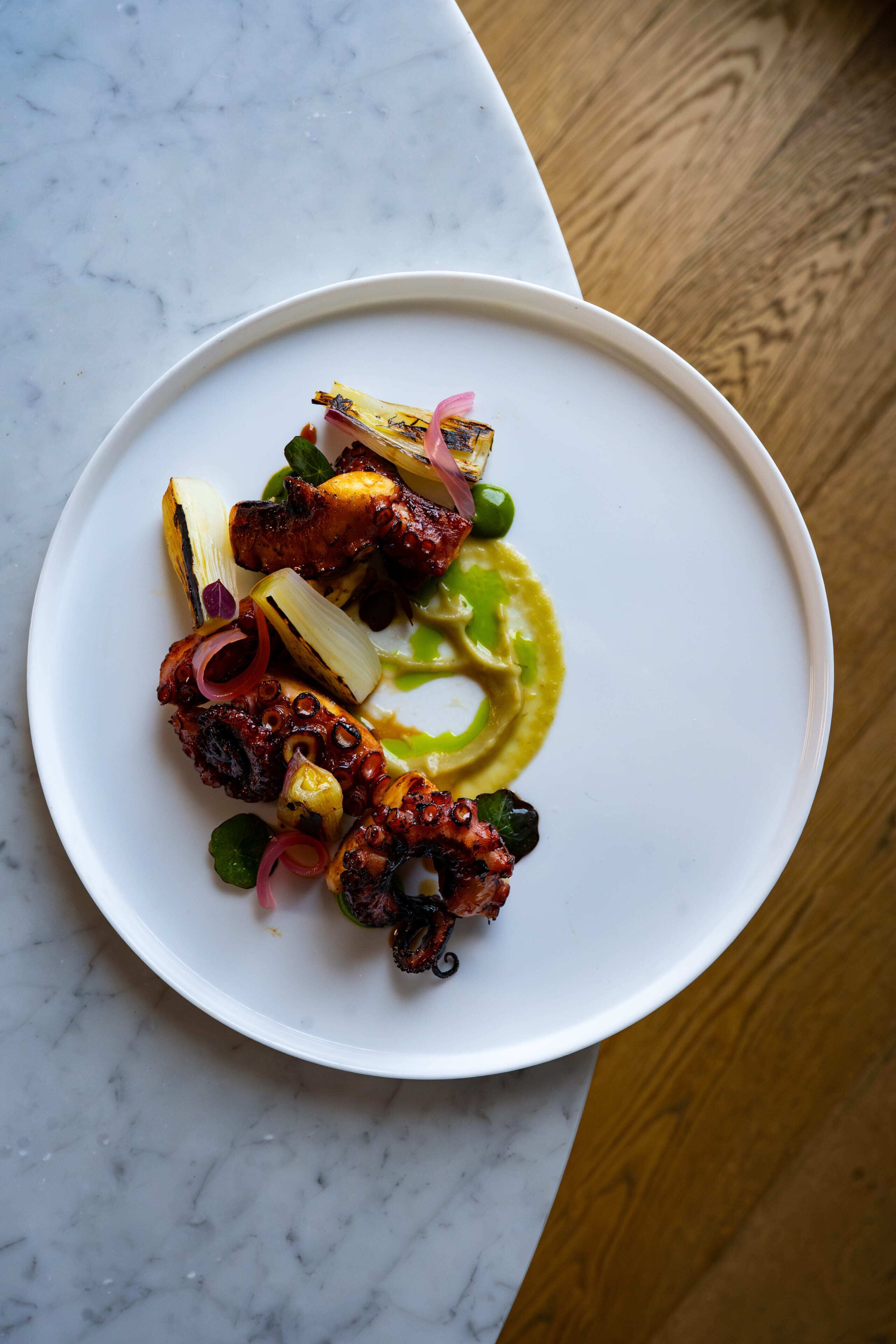 A white plate with a variety of food items including grilled octopus, vegetables, and a green sauce.