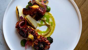 A white plate with a variety of food items including grilled octopus, vegetables, and a green sauce.