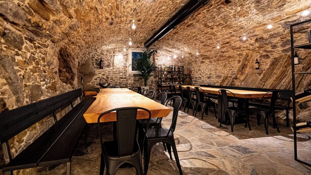 A stone-walled interior with wooden tables and chairs, a bench, and a potted plant. - Locanda Moderna Carlambroeus (Montevecchia)