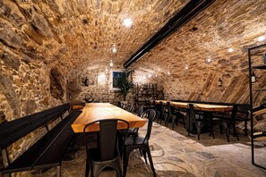 A stone-walled interior with wooden tables and chairs, a bench, and a potted plant.