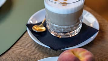 Ein Glas mit einem geschichteten Getränk auf einer Untertasse, zusammen mit einem Löffel und einem Teller mit einem Apfel und einem Pfirsich.