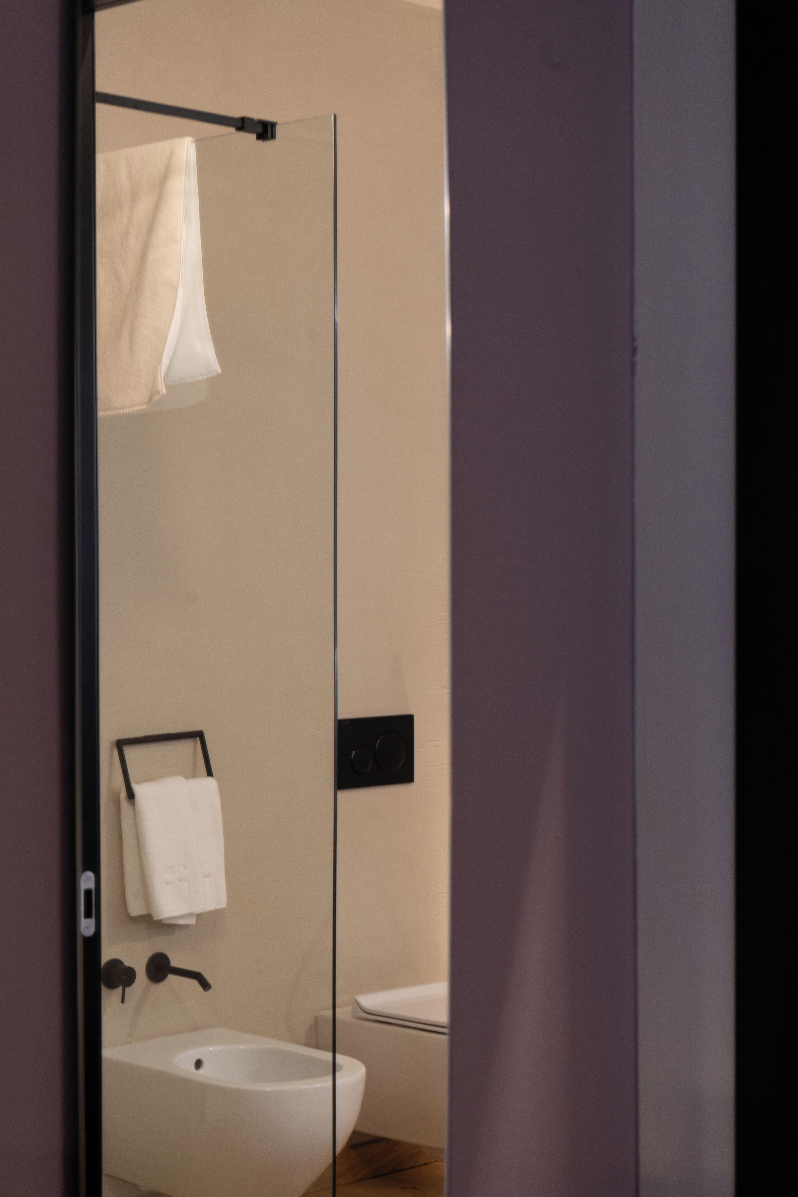 A modern bathroom with a glass shower enclosure, a white sink, and a towel rack.