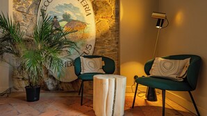 A cozy room with a stone wall, a wooden sign, a potted plant, two green chairs, and a floor lamp. - Locanda Moderna Carlambroeus (Montevecchia)