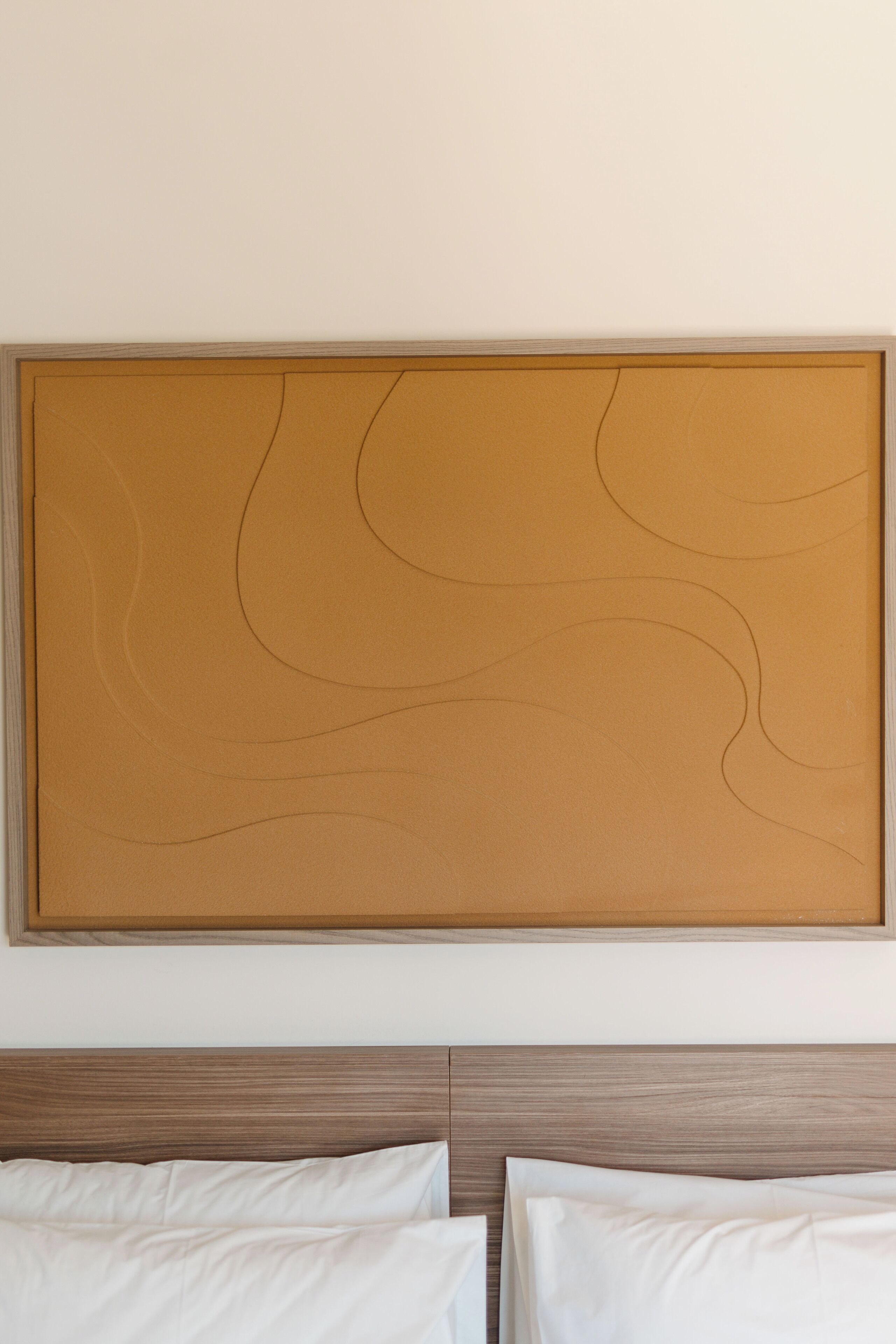 Una habitación con un cuadro abstracto grande en la pared, un cabecero de madera y dos camas blancas.