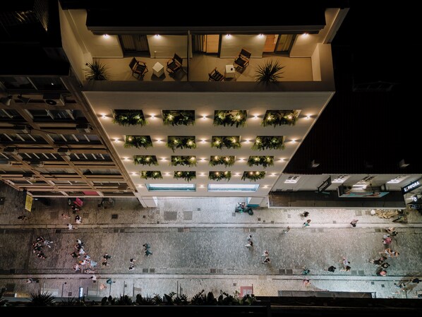 Un edificio moderno con terraza en la azotea que cuenta con varias zonas de estar y plantas en macetas.
