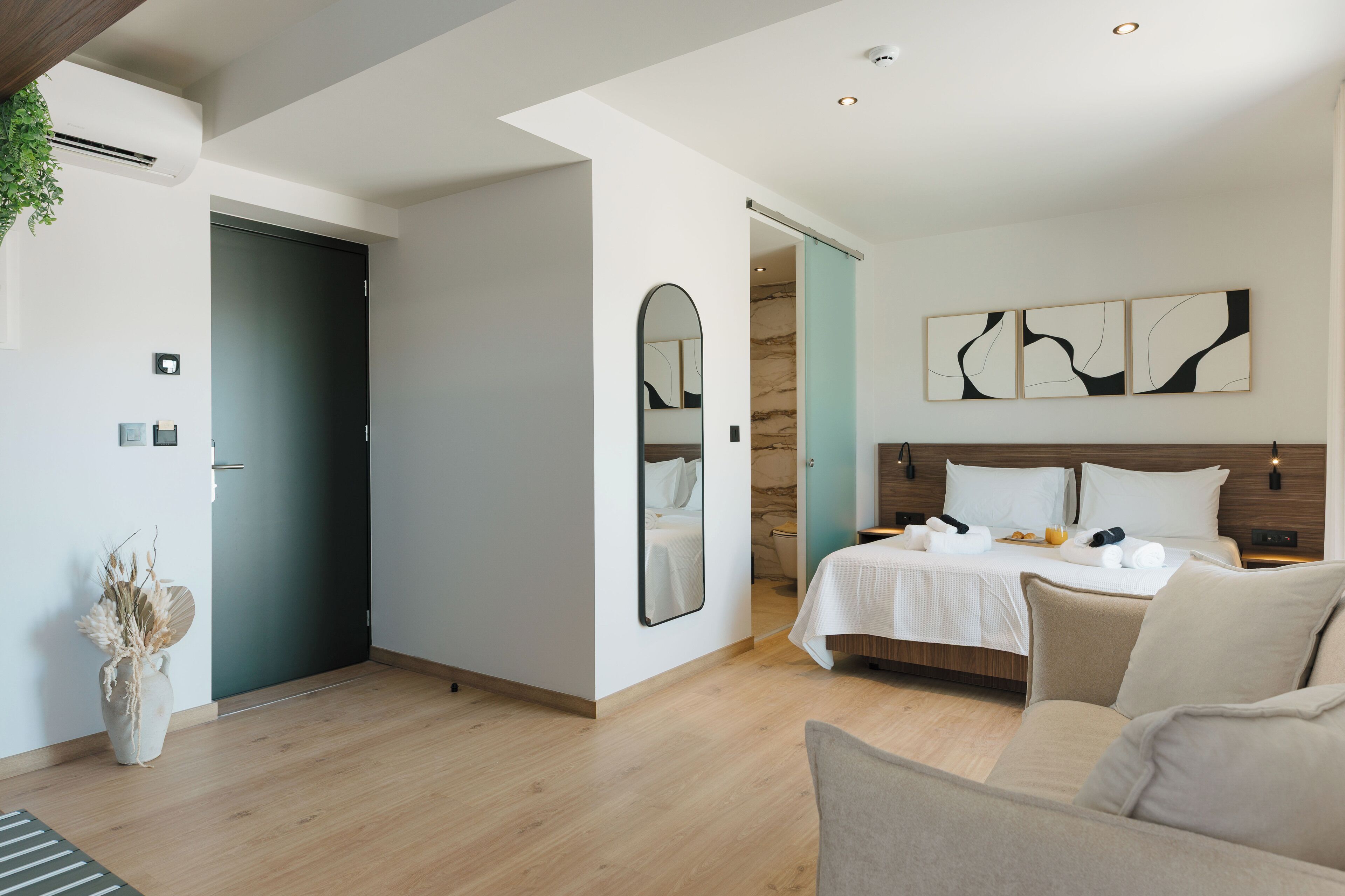 A modern hotel room with a bed, a sofa, a mirror, and abstract wall art.