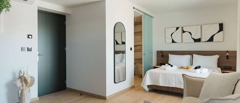 A modern hotel room with a bed, a sofa, a mirror, and abstract wall art.