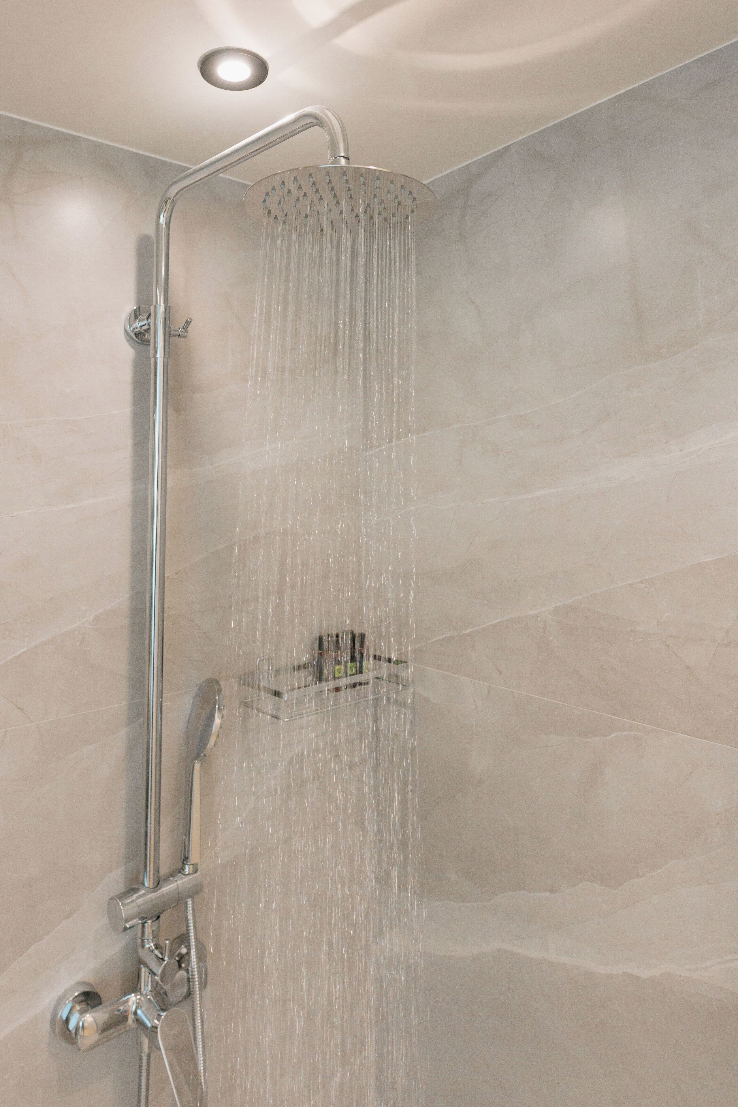 A modern shower with a rain showerhead, a handheld showerhead, and a handheld shower attachment.