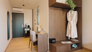 Una habitación de hotel moderna con un escritorio de madera, una bata colgada en un perchero, una planta pequeña y una caja fuerte.