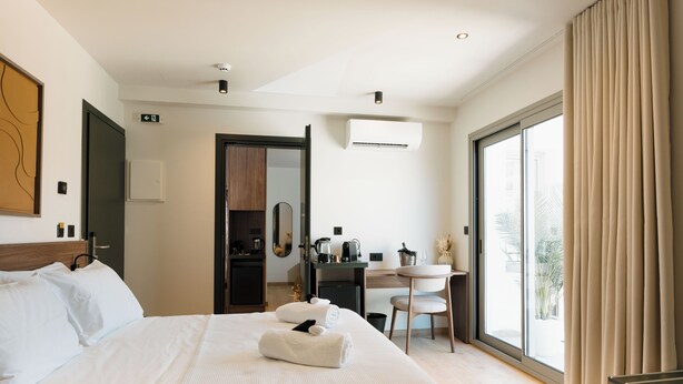 Una habitación de hotel con cama, escritorio, silla, mesita pequeña y un ventanal con cortinas.