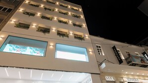 Un edificio de varios pisos con ventanas y balcones iluminados, que cuenta con una gran pantalla digital y señalización para tiendas como Sephora y Ella.
