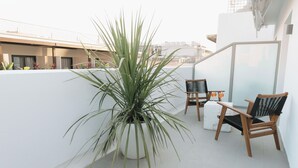 Un balcón con una maceta, dos sillas de madera y una mesa blanca.